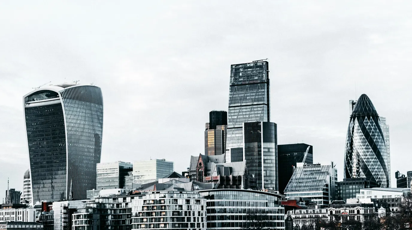 A dense cluster of glass and steel towers under a flat white sky, the whole view drained to cool greys.